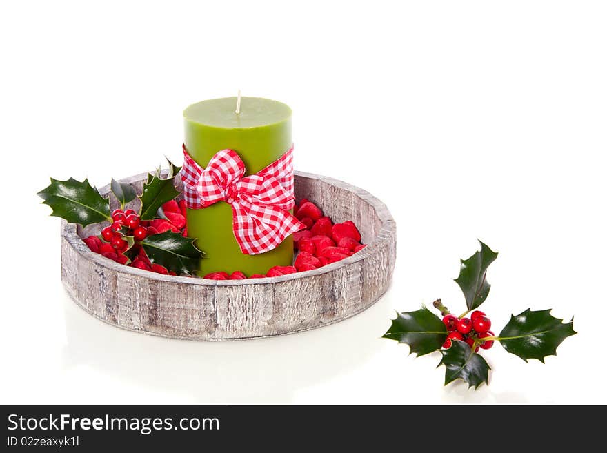 A green candle decorated with stones and holly on a wooden tray isolated over white