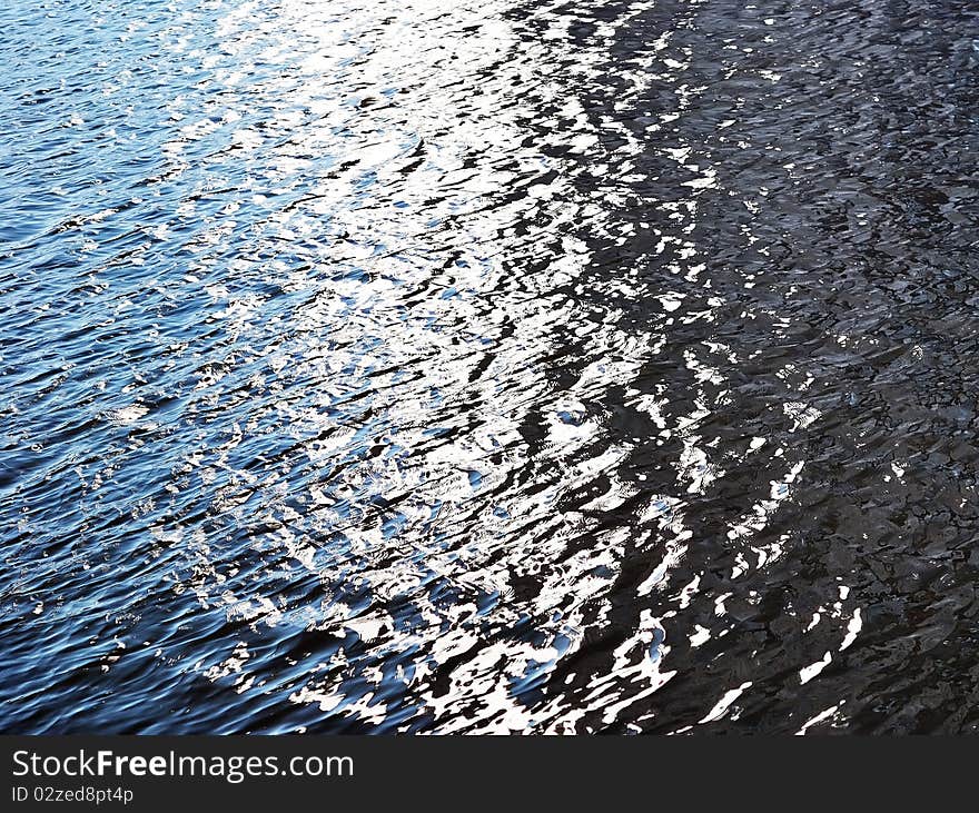 Abstract background photo of a river water surface with patches of sunlight ripple and whirlpools