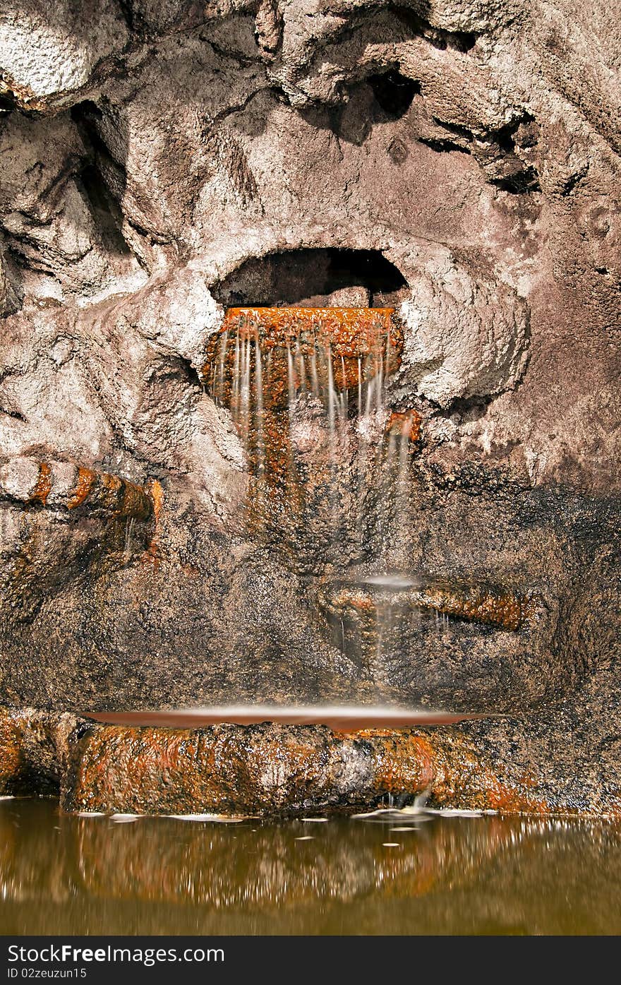 A waterfall spilling water onto a pond inside of a cave. A waterfall spilling water onto a pond inside of a cave.