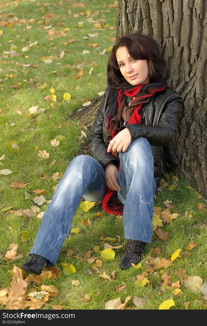 Girl sitting under the tree in an autumn park