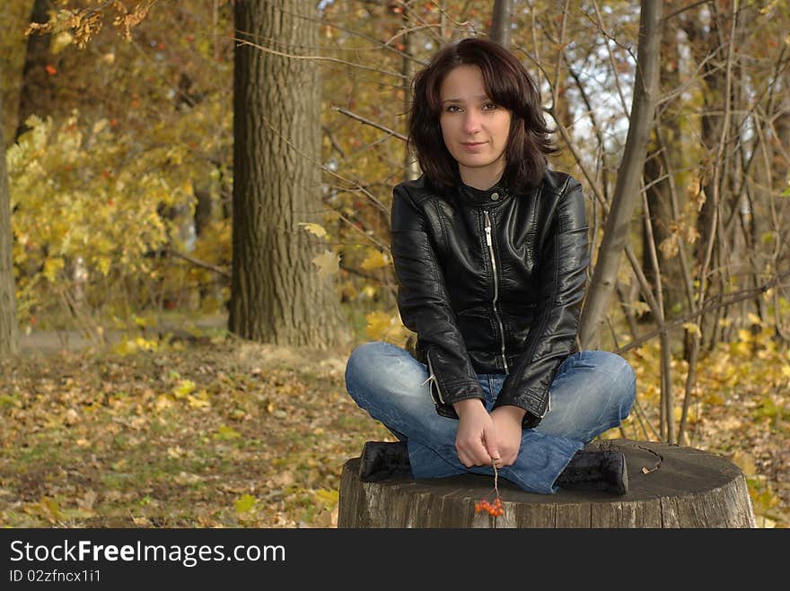 Girl sitting cross-legged on a stump in the autumn forest