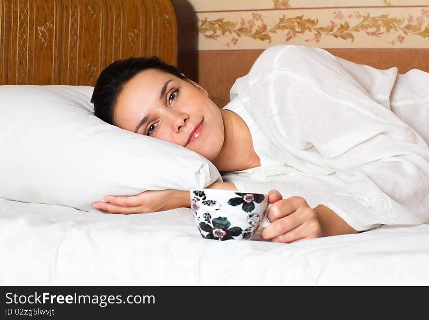 Woman lying in bed and tasting coffee