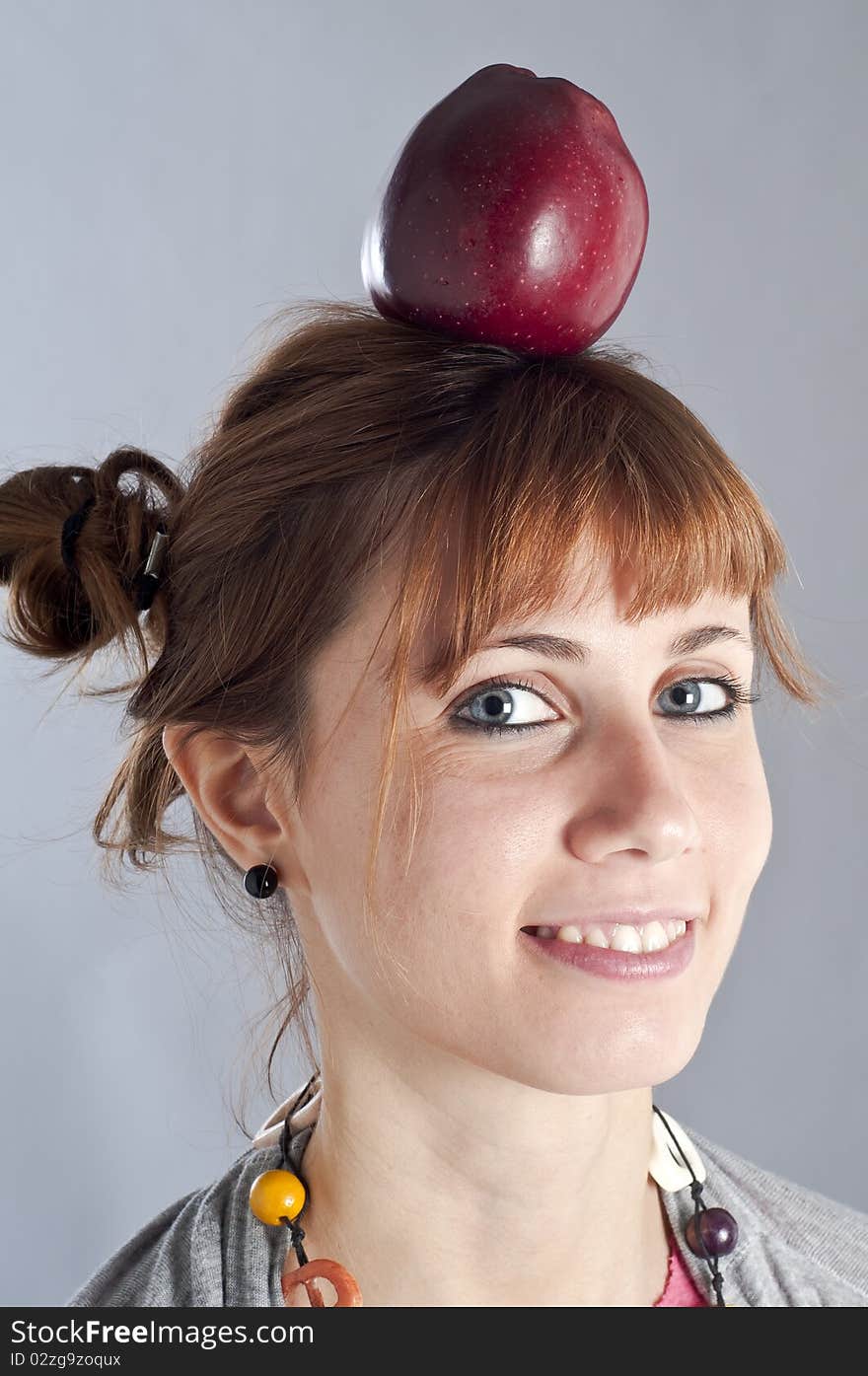 Young girl with pigtails, and colorful necklace and an apple on her head. Young girl with pigtails, and colorful necklace and an apple on her head