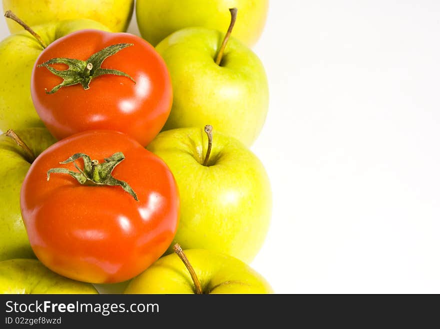 Two rows of green apples are placed vertically on the left of the image. on top of them are two red tomatoes. Two rows of green apples are placed vertically on the left of the image. on top of them are two red tomatoes