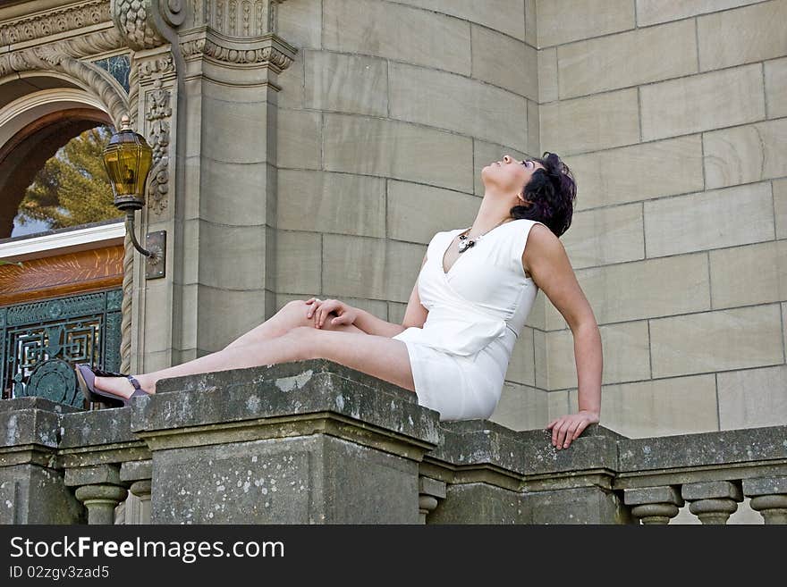 A woman in white dress reclining on a stone railing. A woman in white dress reclining on a stone railing.