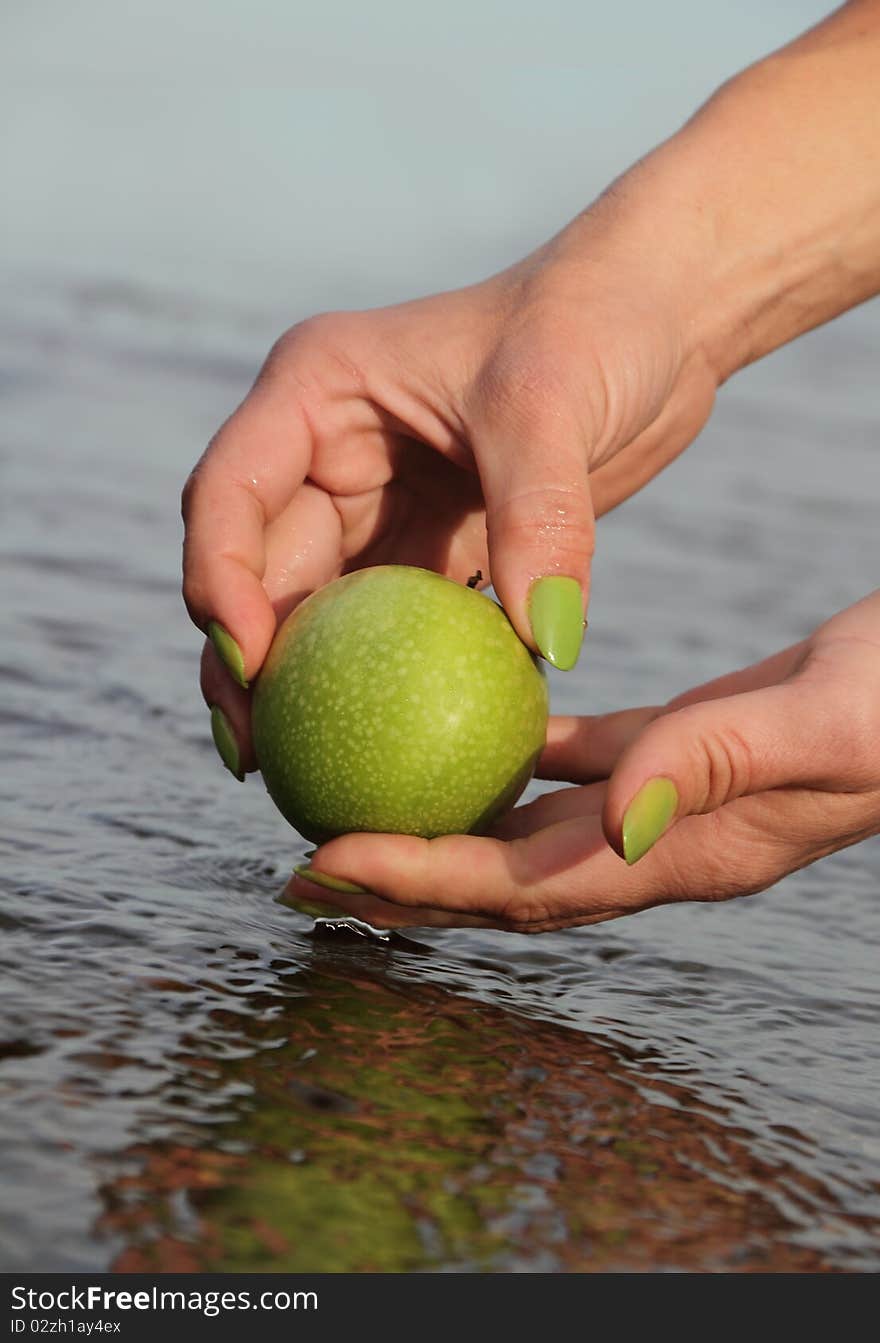 Hands cleaning apple in water.