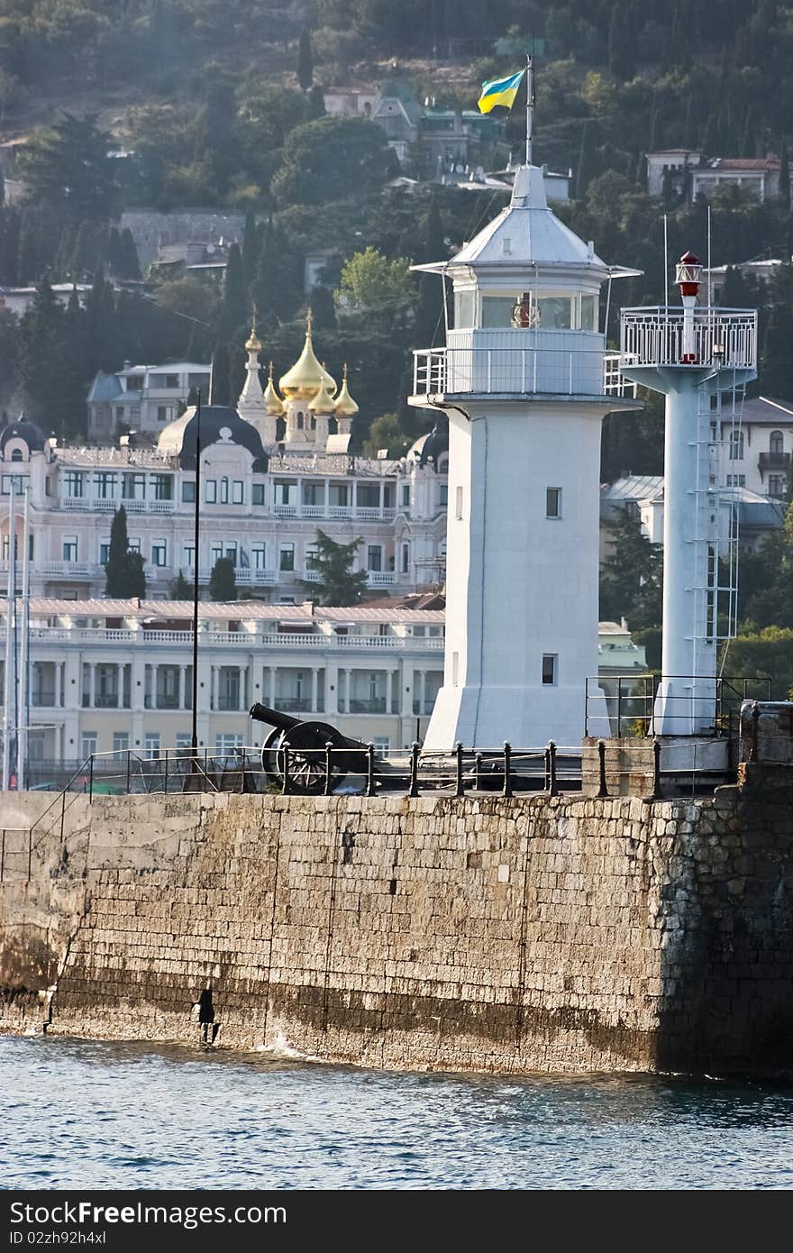 Coastal beacon with an artillery gun on the stone basis at the sea, on a back background of a building, gold domes of church. Coastal beacon with an artillery gun on the stone basis at the sea, on a back background of a building, gold domes of church