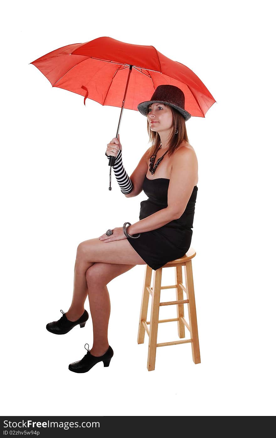 An middle aged woman in an short black dress and a gray hat sitting in the studio with a red umbrella in her hand. An middle aged woman in an short black dress and a gray hat sitting in the studio with a red umbrella in her hand.