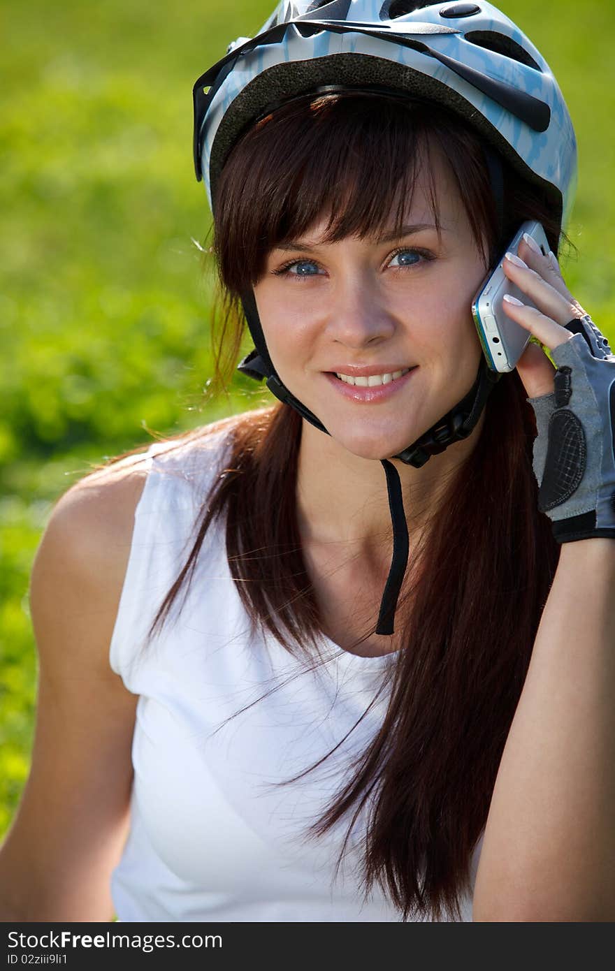 Young female cyclist making a call on the grass background