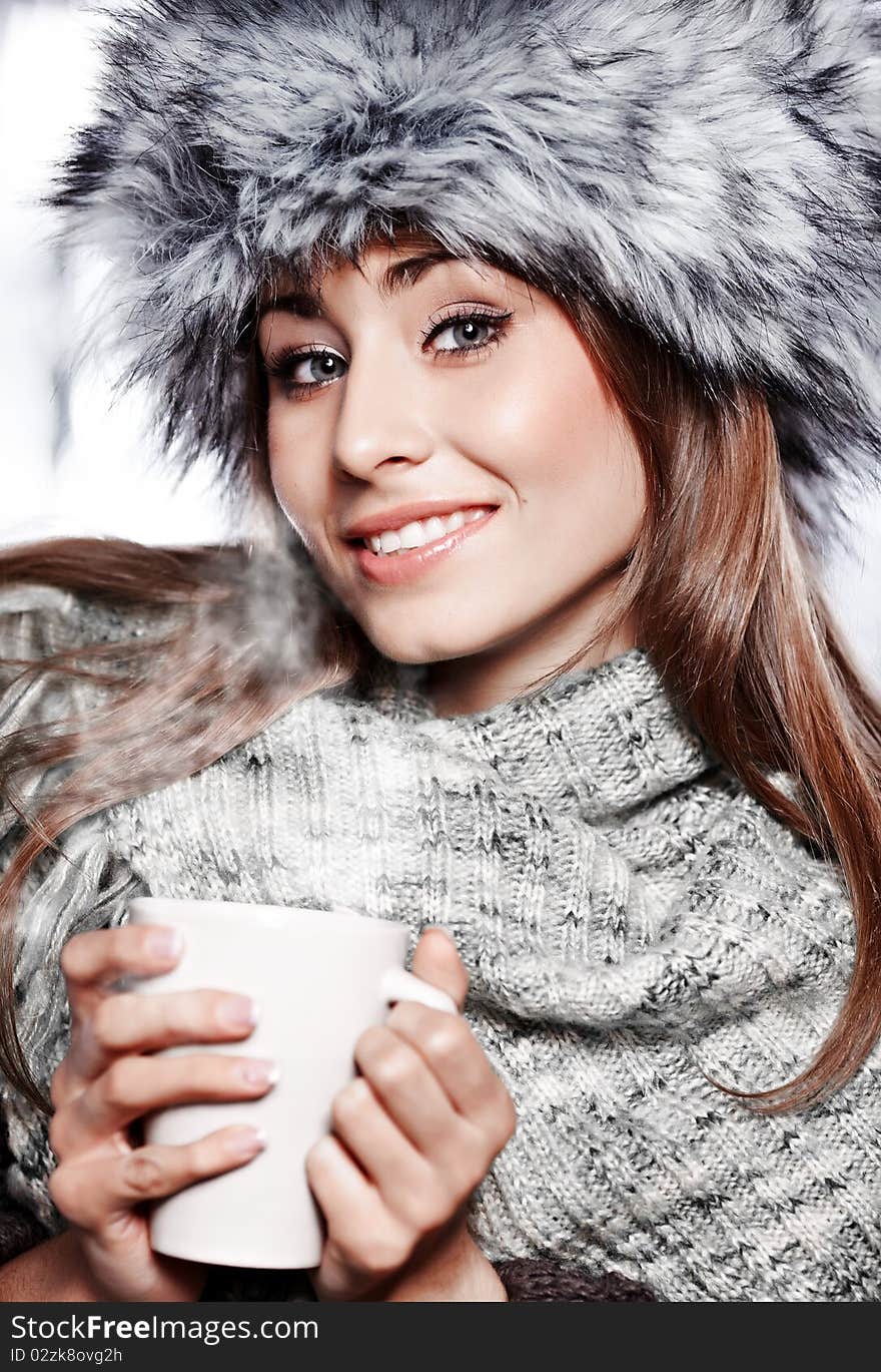 Girl blowing on hot drink dressed in winter clothing