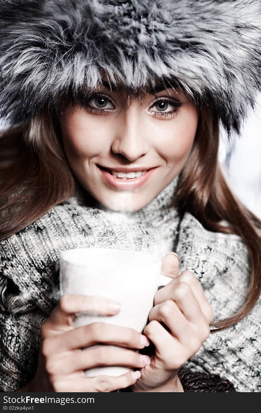 Girl blowing on hot drink dressed in winter clothing