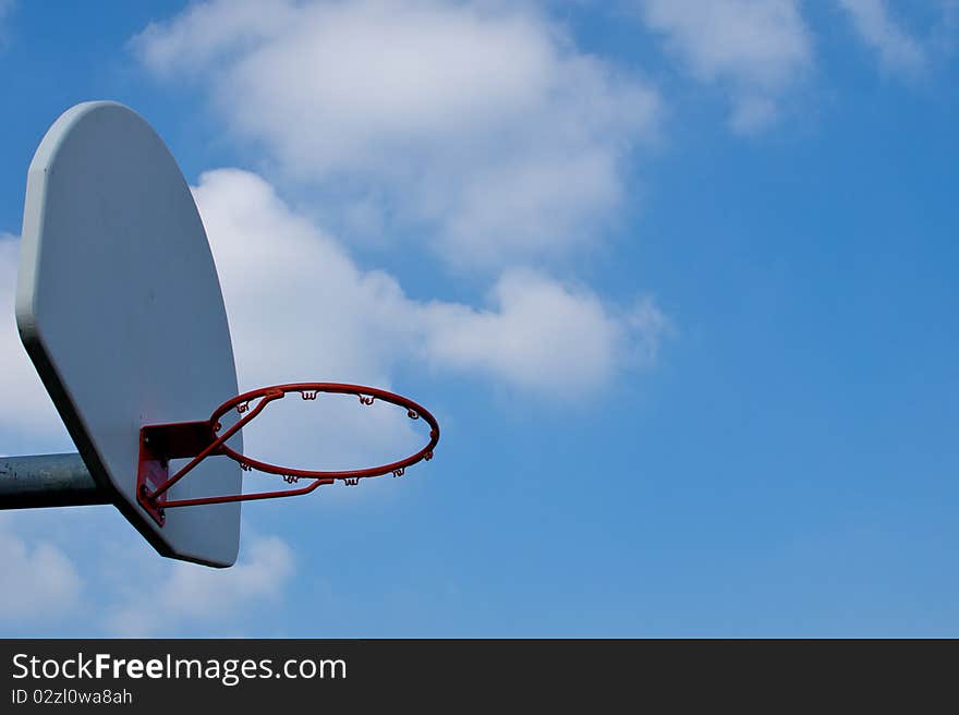 An empty basketball hoop against a bright blue sky, with large clouds drifting from behind the backboard. An empty basketball hoop against a bright blue sky, with large clouds drifting from behind the backboard.