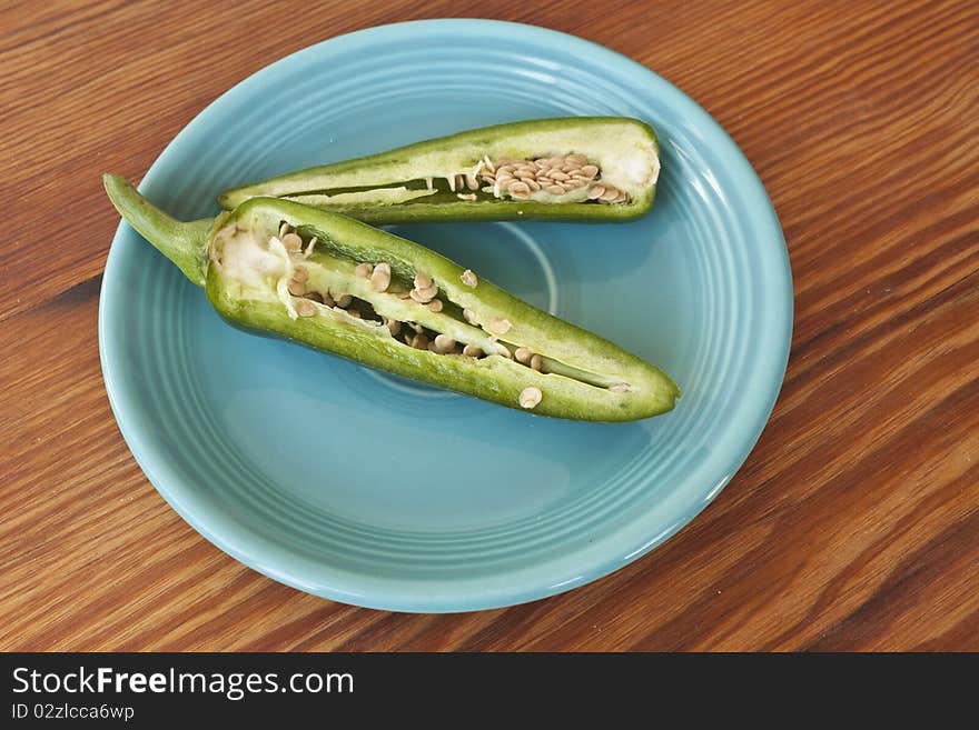 Jalepenos cut in half with seeds showing in a turquioise plate on a wooden table. Jalepenos cut in half with seeds showing in a turquioise plate on a wooden table.