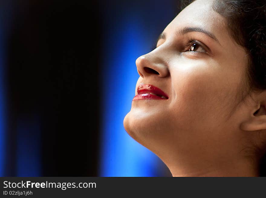 High contrast, portrait of a smiling young Indian woman. Blue light background. High contrast, portrait of a smiling young Indian woman. Blue light background