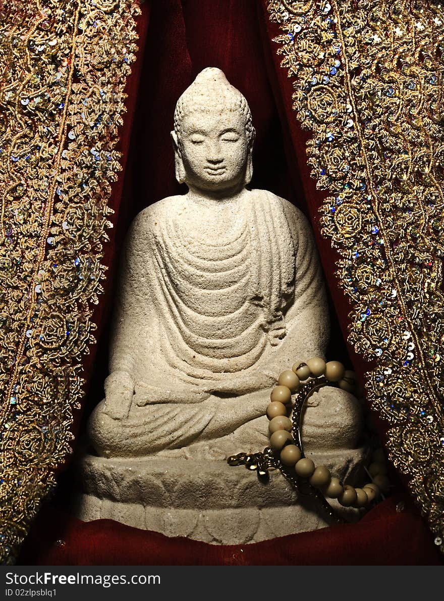 A stone statue of a buddha meditating in between indian material. A stone statue of a buddha meditating in between indian material.