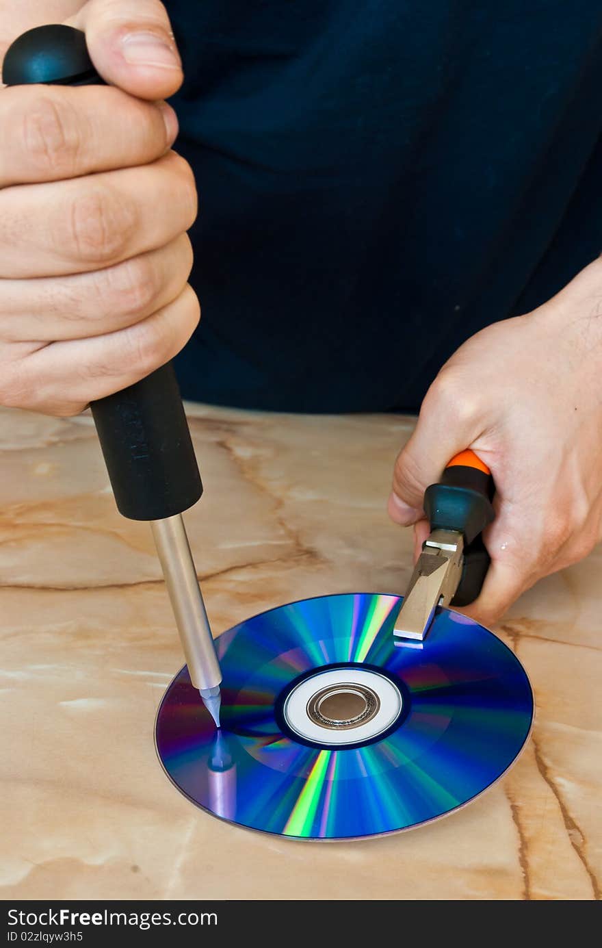 Man destroying a compact disc with a screwdriver. Man destroying a compact disc with a screwdriver