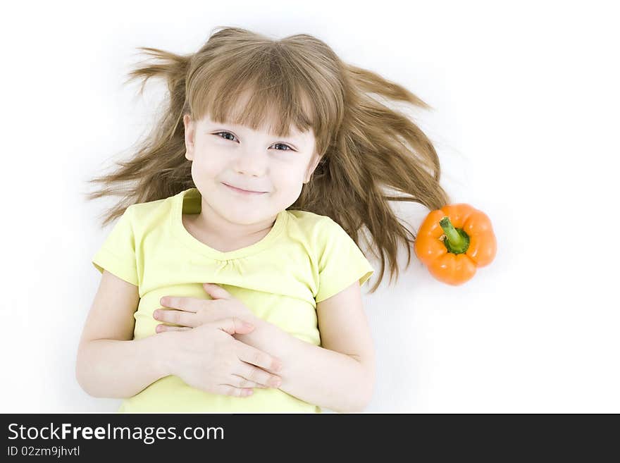 The portrait of a happy little girl lying on the floor with fresh vegetable