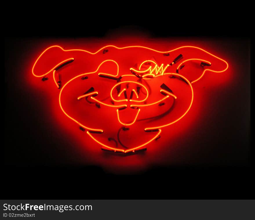 Illuminated, orange glowing pig neon sign for butcher shop on black background at night time. Illuminated, orange glowing pig neon sign for butcher shop on black background at night time