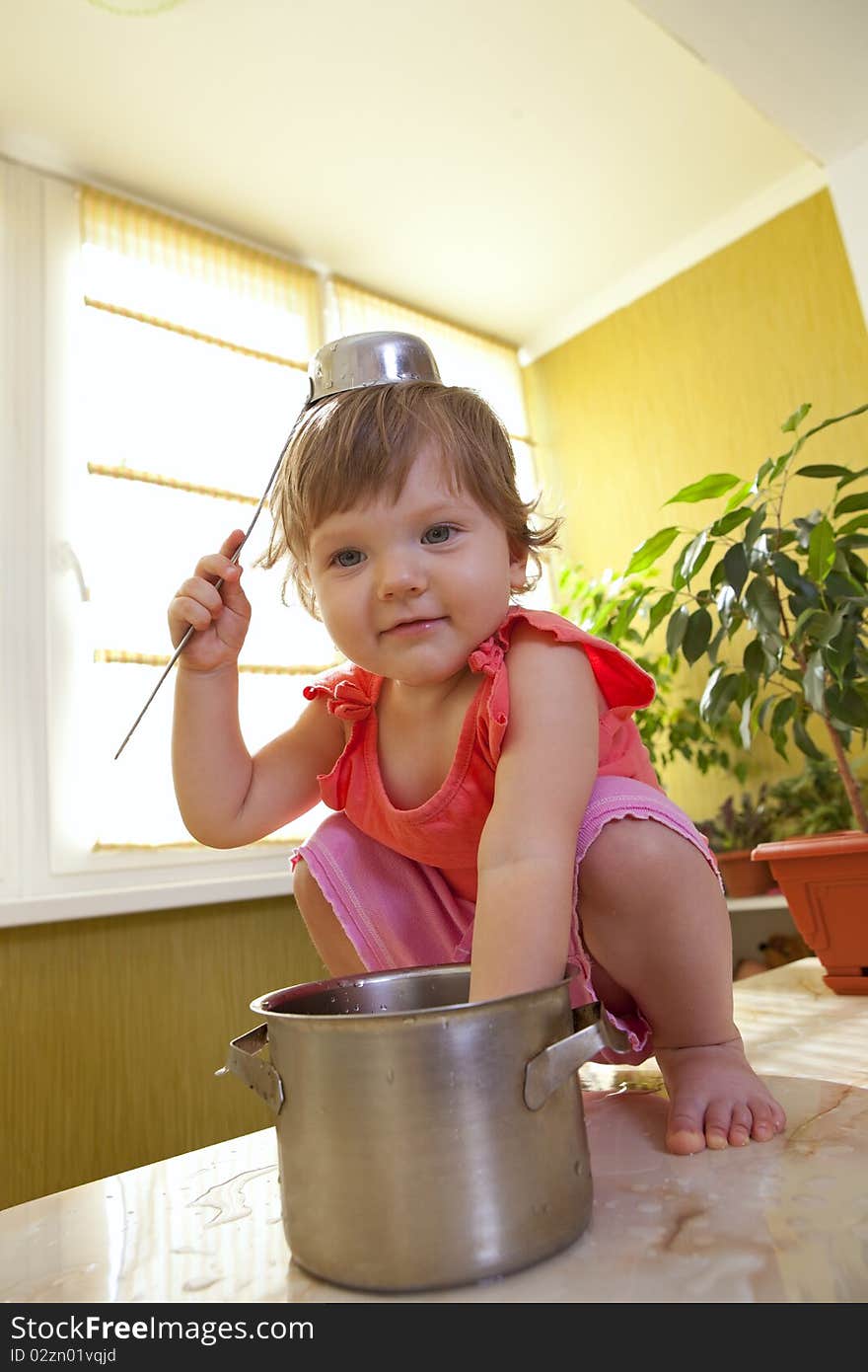 Little girl with a pan and ladle on her head sitting on a table