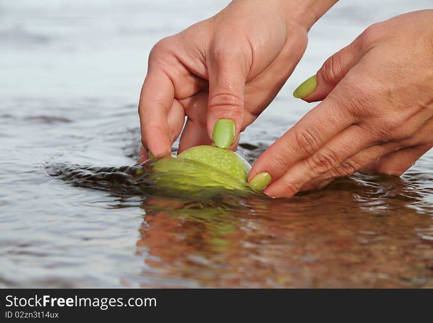 Hands cleaning apple in water.