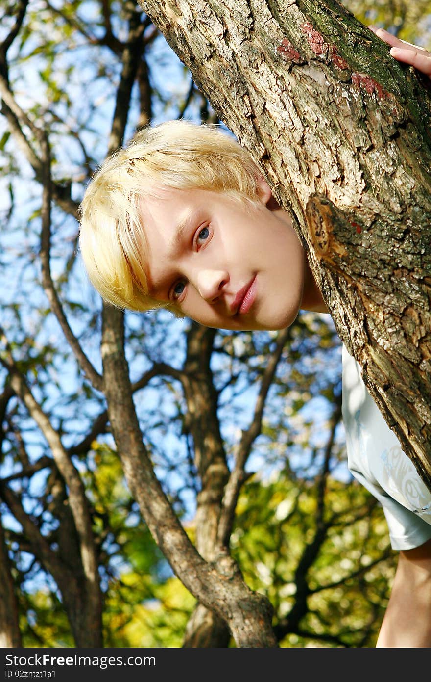 Attractive blond guy behind a tree in park