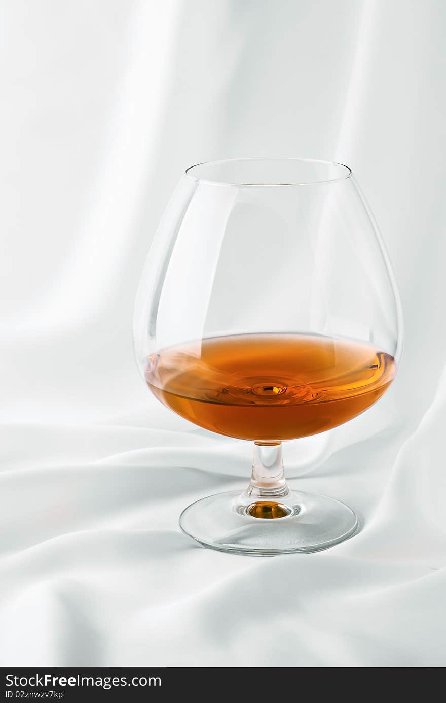 Glass of cognac on white silk. Glass of cognac on white silk