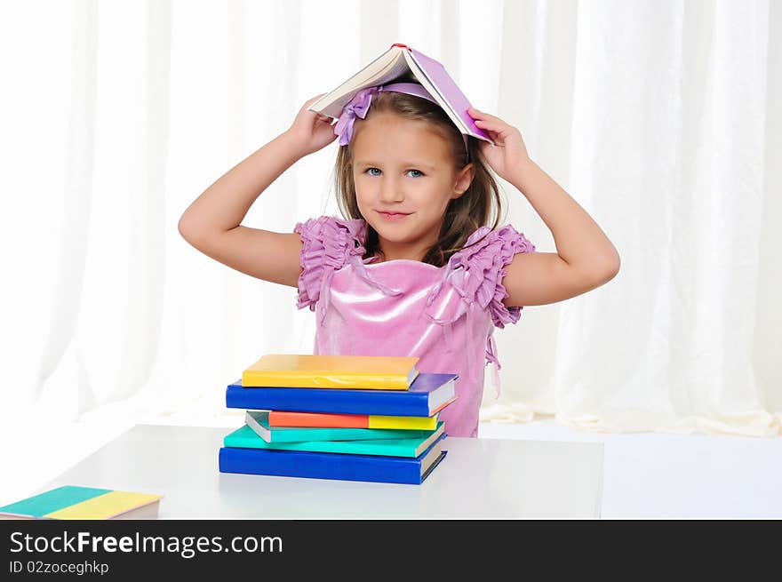 The little girl is studying literature. Reads a book while sitting at a white table.