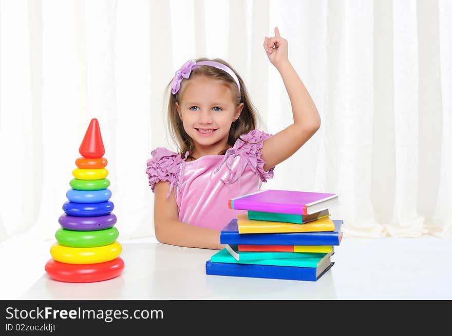 The little girl is studying literature. Reads a book while sitting at a white table.