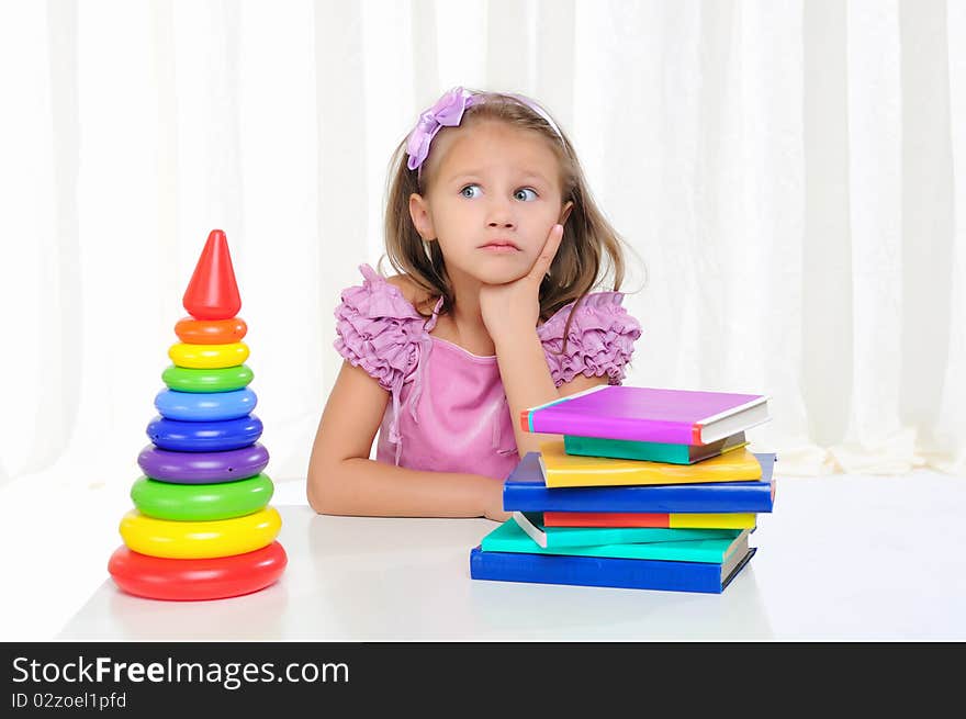 The little girl is studying literature. Reads a book while sitting at a white table.