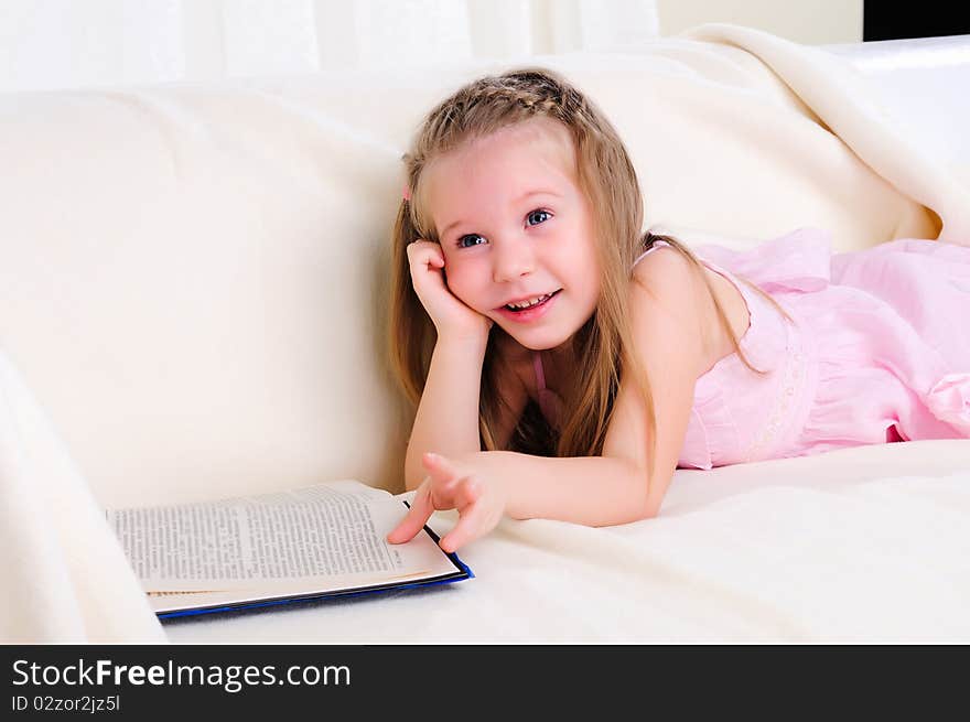 Little girl lying on the couch reading a book