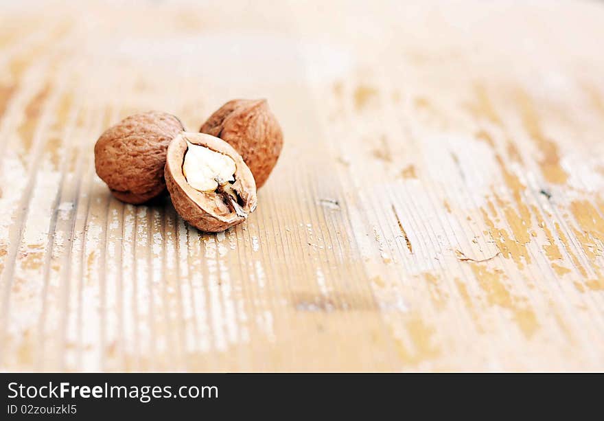 Three walnuts are two whole and one halved on wooden backgroun