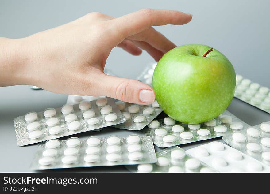 Female hand holds an apple against the scattered tablets. Female hand holds an apple against the scattered tablets