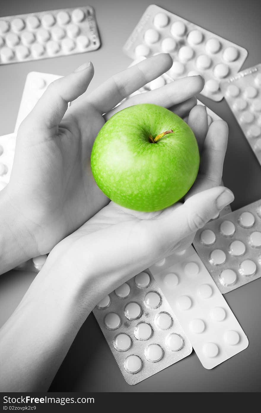 Female hands holds an apple against the scattered tablets. Black-and-white. Female hands holds an apple against the scattered tablets. Black-and-white