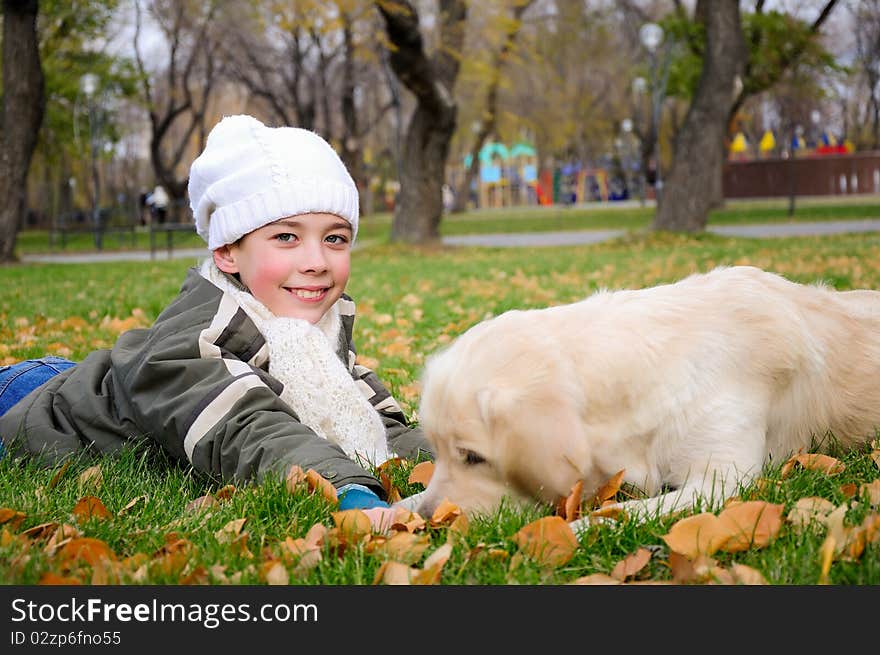 Boy playing in autumn park with a golden retriever.