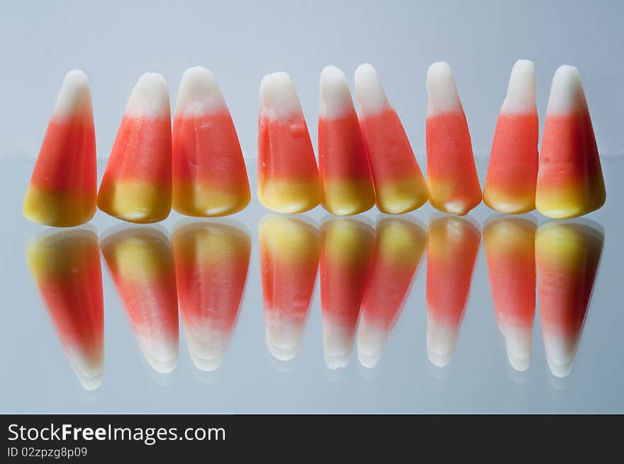 Nine pieces of candy corn standing upright, on white background, with corn pieces reflection. Nine pieces of candy corn standing upright, on white background, with corn pieces reflection.