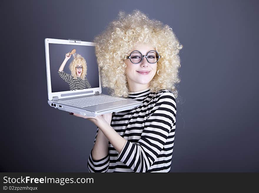 Portrait of funny girl in blonde wig with laptop. Studio shot.