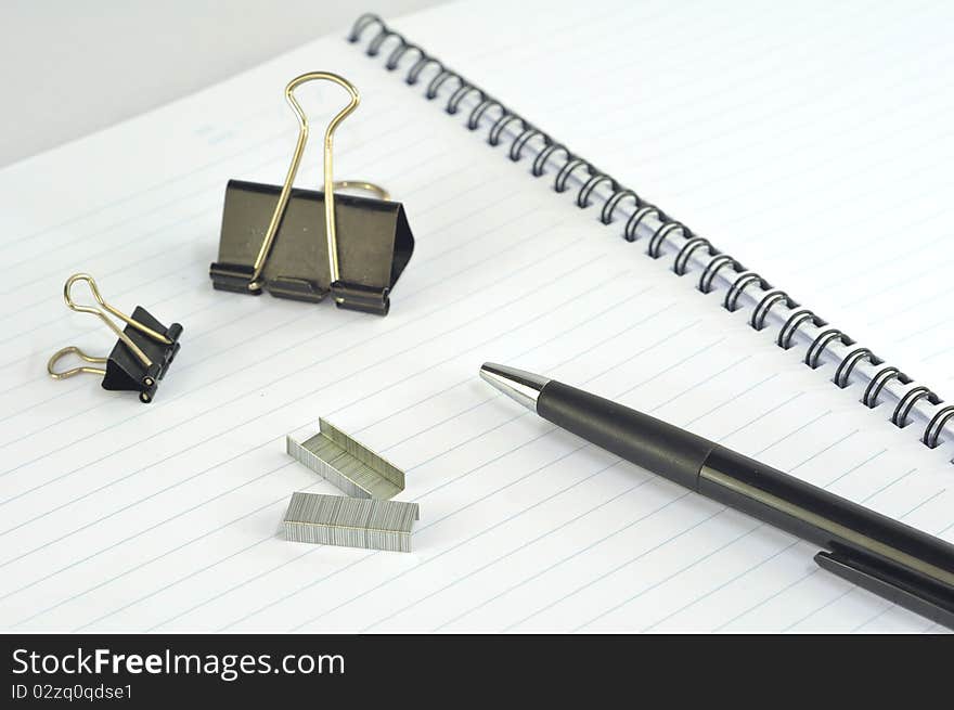 Empty spiral notebook with paper clip, pencil and pen on white background