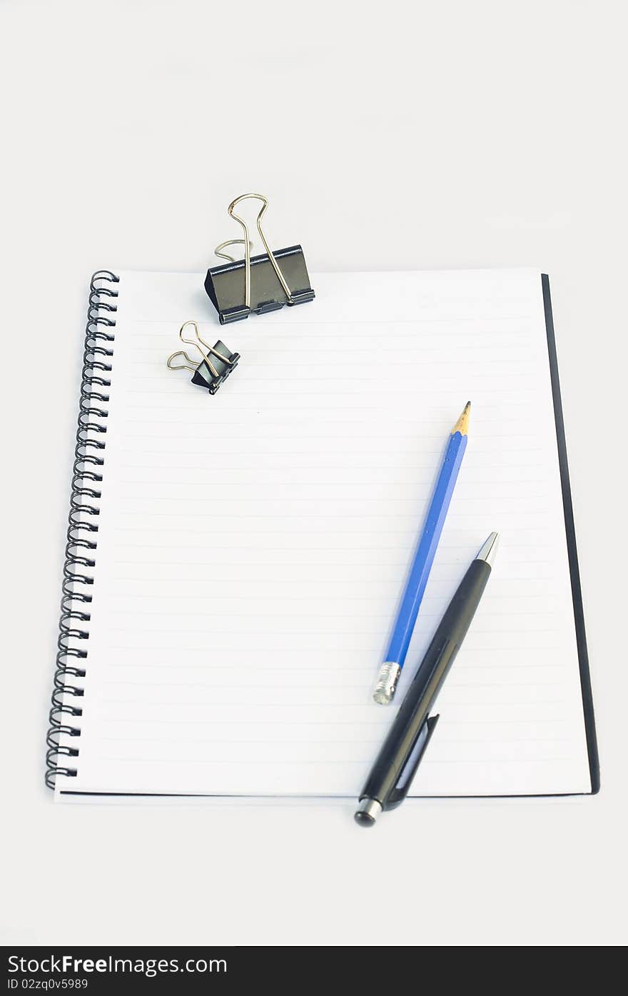 Empty spiral notebook with paper clip, pencil and pen on white background