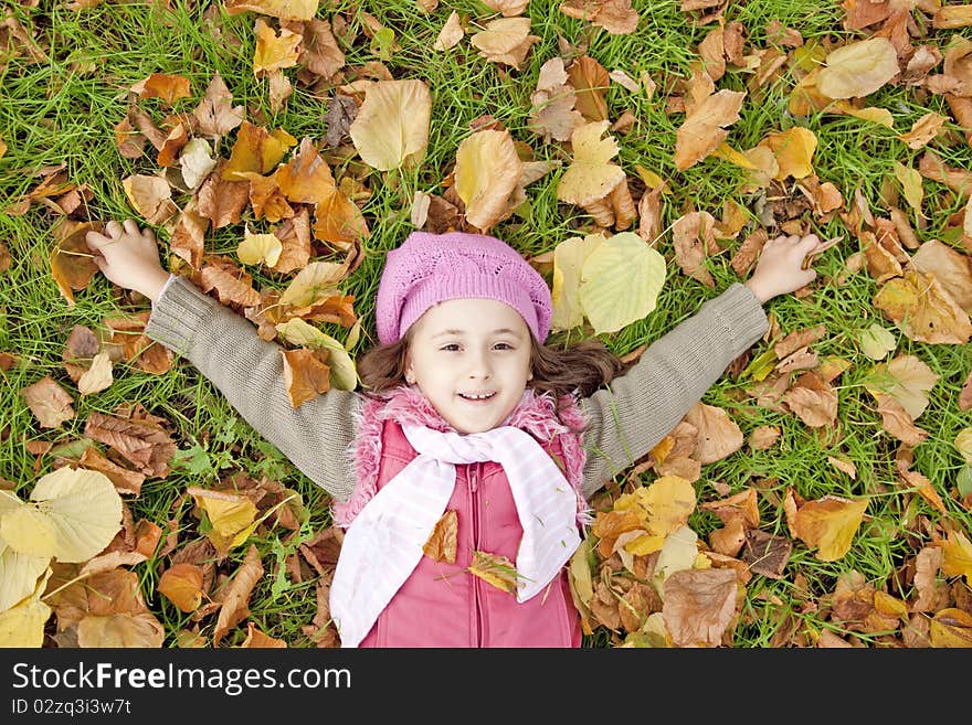 Little girl at grass and leafs in the park.