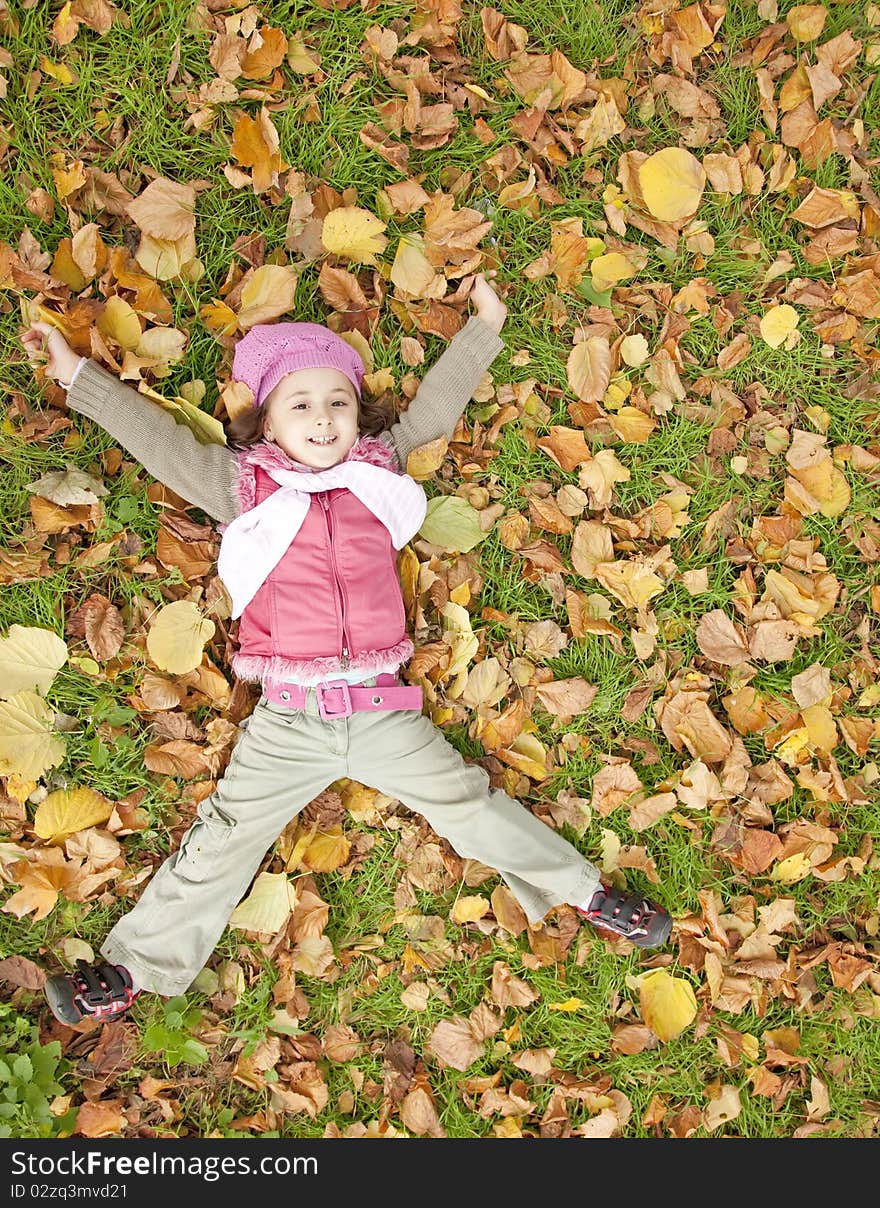 Lying down little girl at grass and leafs in the park. outdoor shot.