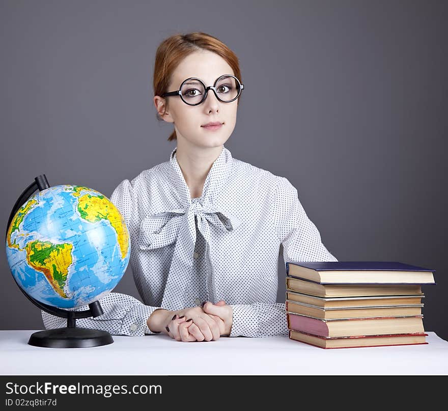 The young teacher in glasses with books and globe. Studio shot.