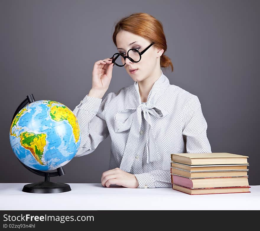 The young teacher in glasses with books and globe. Studio shot.