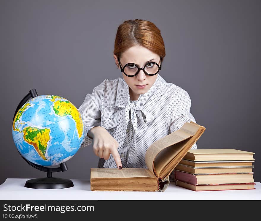 The young teacher in glasses with books and globe. Studio shot.