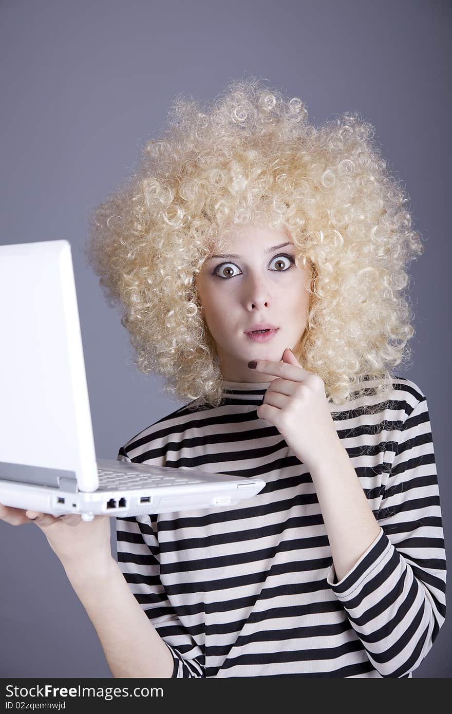 Portrait of funny girl in blonde wig with laptop. Studio shot.