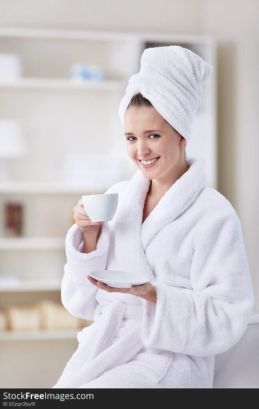 A beautiful young girl in a bathrobe and a towel with a cup of coffee. A beautiful young girl in a bathrobe and a towel with a cup of coffee