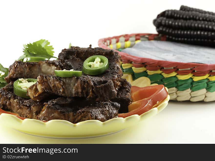 Beef short ribs barbecued with Mexican adobe sauce on a plate with jalapeno peppers and cilantro garnish and blue corn tortillas in a basket. Beef short ribs barbecued with Mexican adobe sauce on a plate with jalapeno peppers and cilantro garnish and blue corn tortillas in a basket.