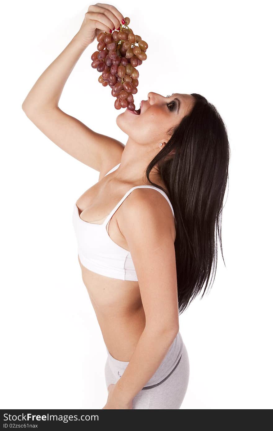 A woman in a white sports bra is eating grapes. A woman in a white sports bra is eating grapes.