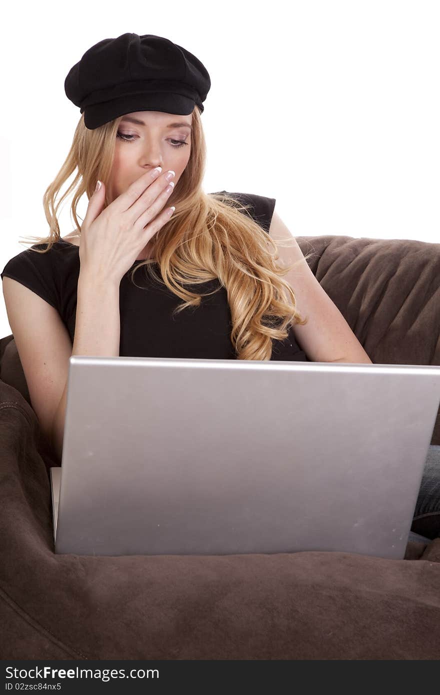 A woman in a black hat is yawning and using a computer. A woman in a black hat is yawning and using a computer.