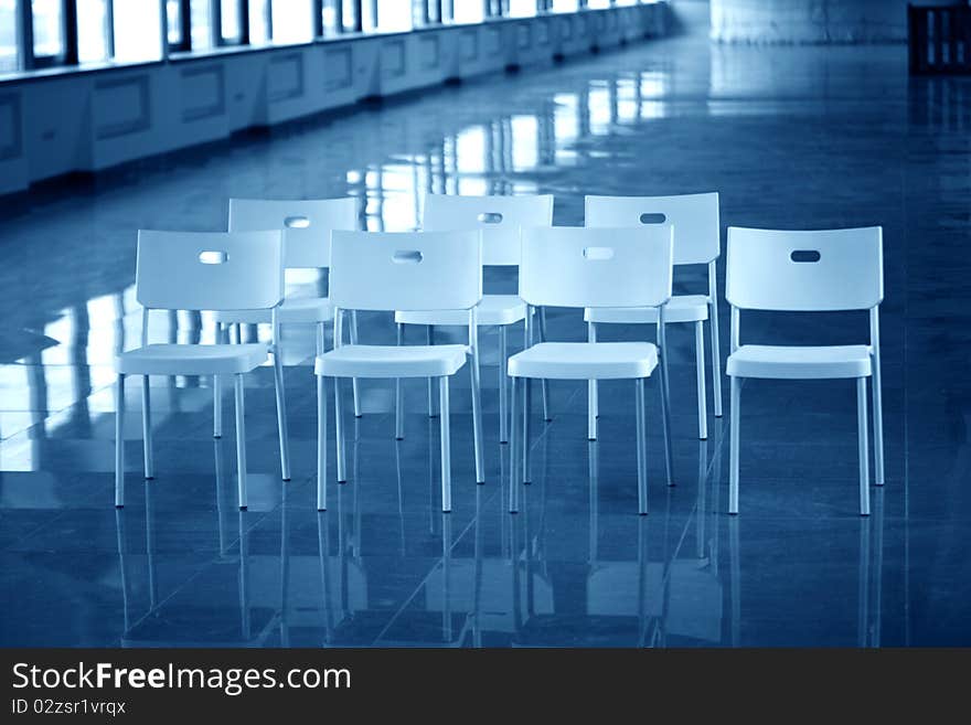 Few white plastic chairs standing in big hallway. Blue tone. Few white plastic chairs standing in big hallway. Blue tone