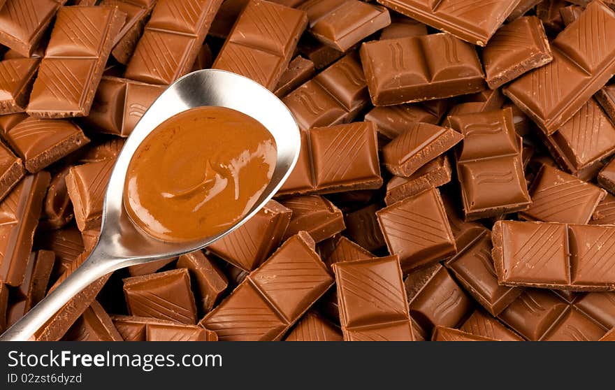 Broken pieces of chocolate as a background with a silver spoon. Broken pieces of chocolate as a background with a silver spoon